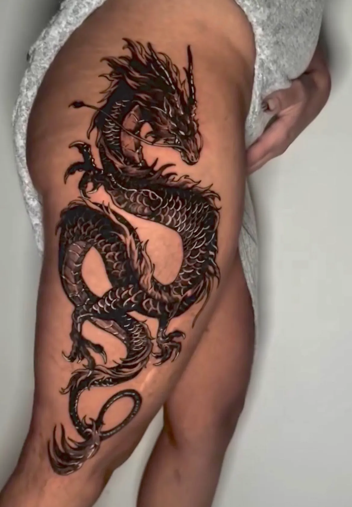 Dragão oriental de corpo escamado enrolado sobre si mesmo, da anca ao joelho